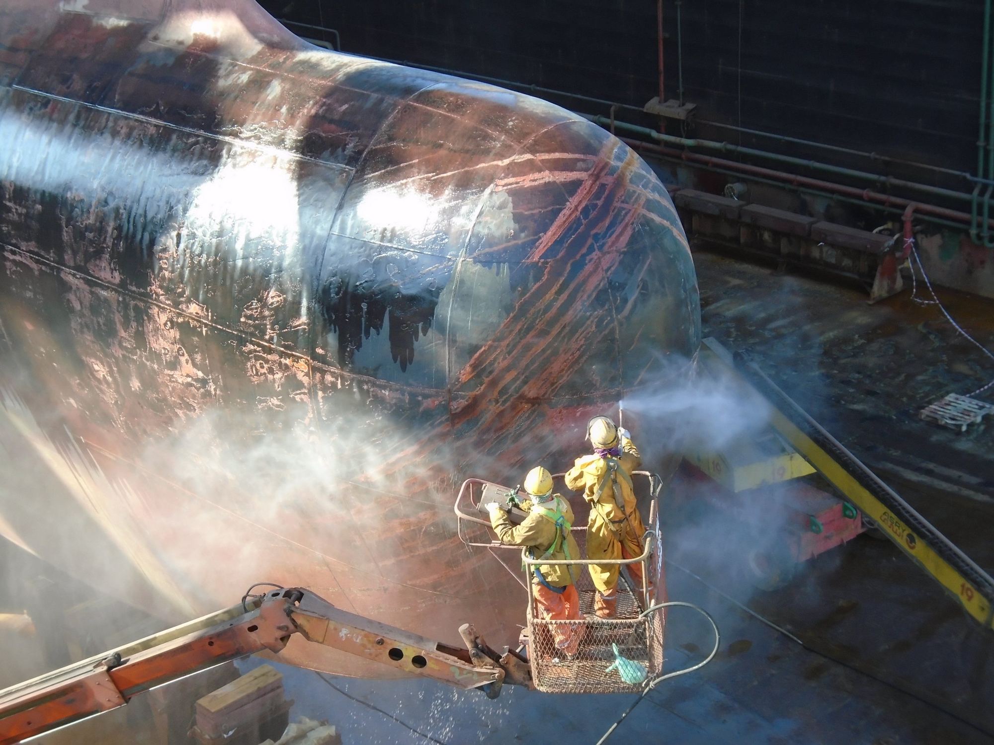 Premator Gulf operators UHP water jetting a ship's bulbous bow from a boom lift in dry dock