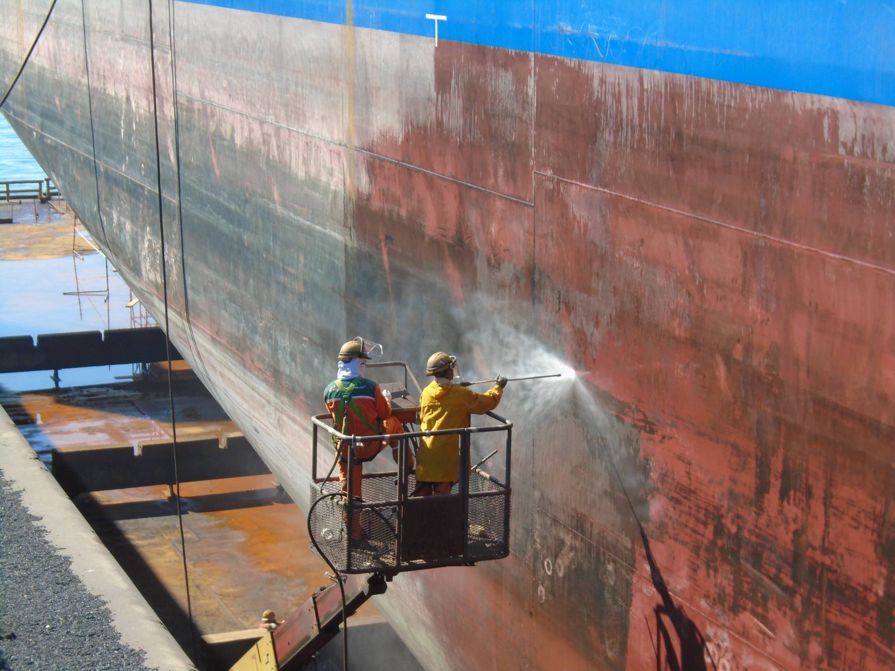 Premator Gulf operators UHP water jetting a ship's hull from a boom lift in dry dock
