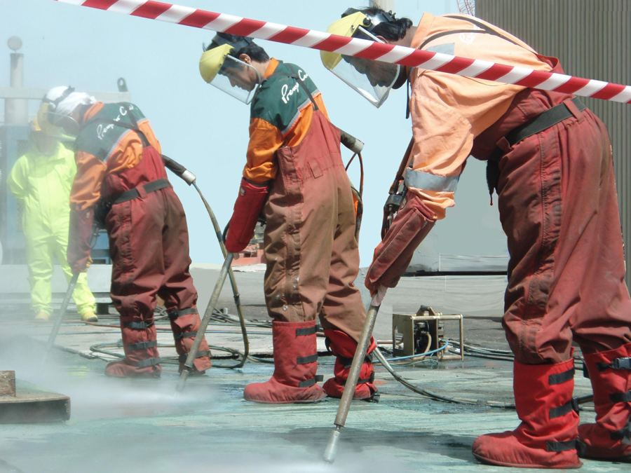 Three Premator Gulf operators high-pressure washing a steel surface