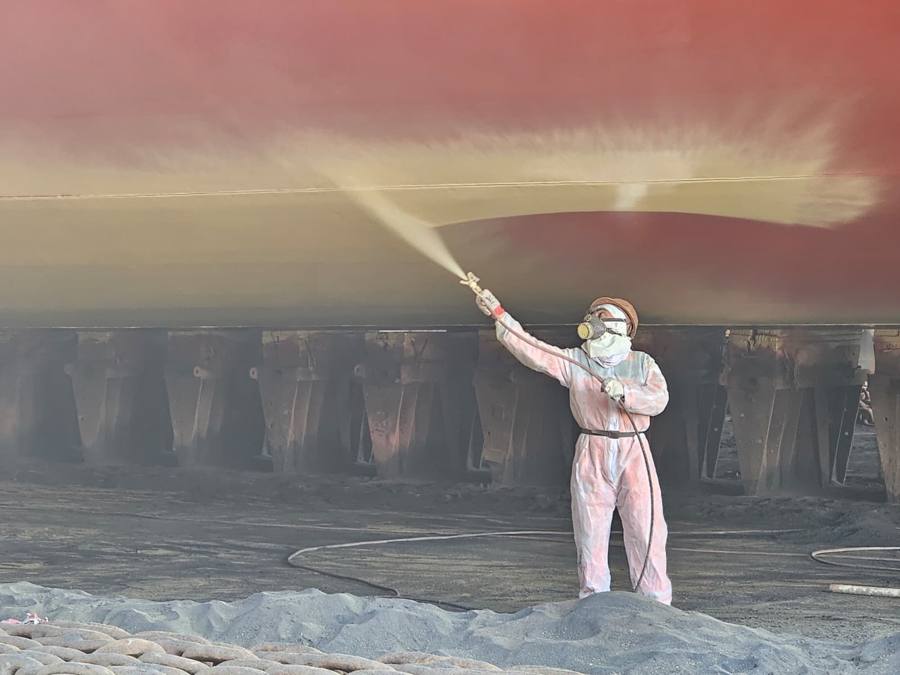Operator in protective suit spray-blasting beneath a hull