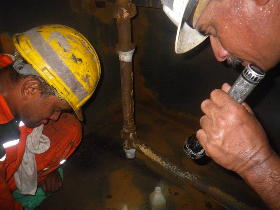 Inspector checking corroded pipework inside a tank